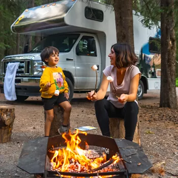 mom and son around fire pit while camping with rv